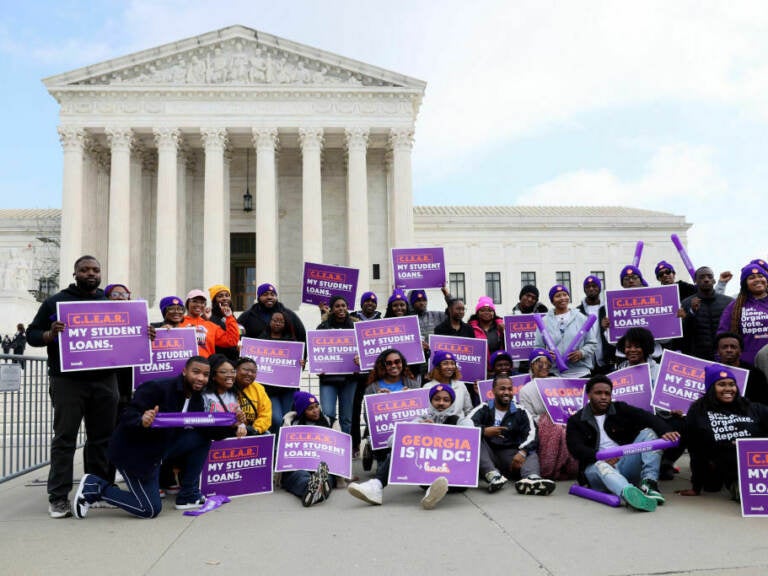 A group of people hold signs in front of the U.S. Supreme Court.