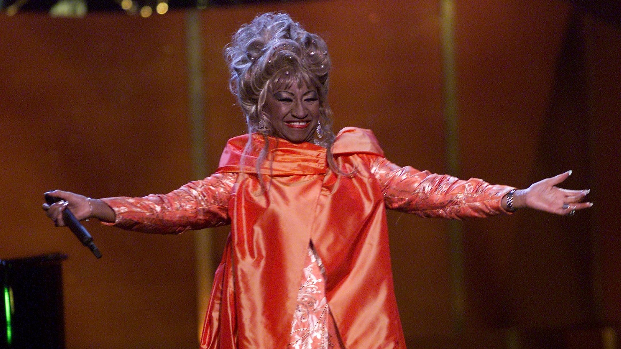 Celia Cruz spreads her arms wide as she poses on stage.