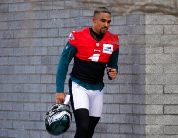 Jalen Hurts, wearing a red practice jersey, walks by a brick wall.