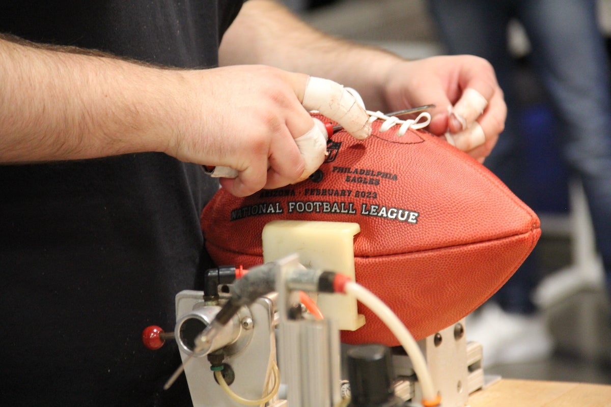 An up-close photo of a person tying the seams on a football.