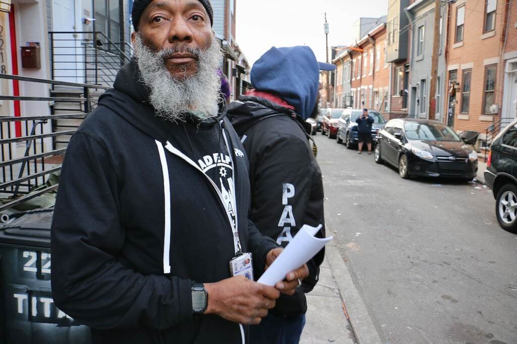 A close-up of a person holding a brochure. Houses are visible in the background. 