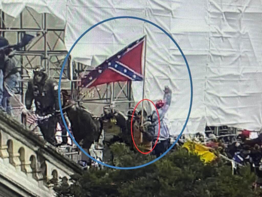 A grainy image of a person waving a Confederate flag on Jan. 6