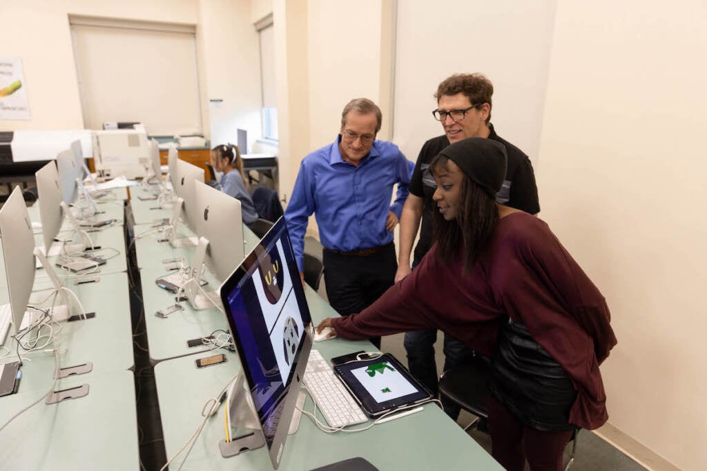 A group of people look at a computer screen in a computer lab.