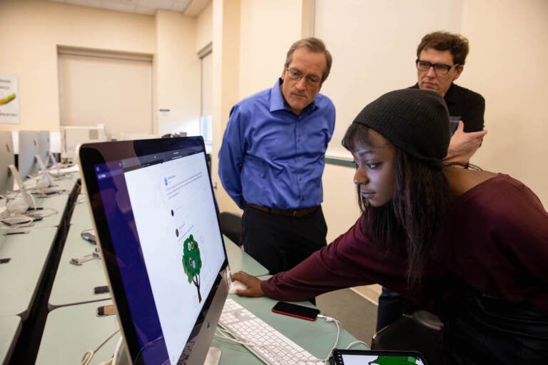 A student looks at a screen as two professors look on behind her.