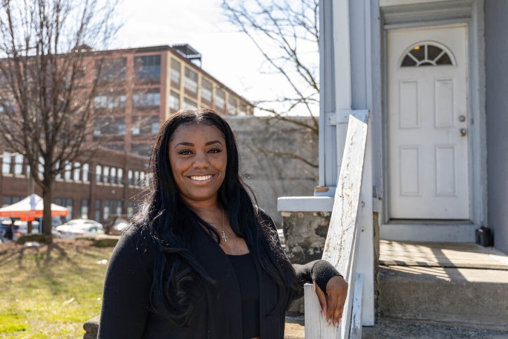 Salima Cunningham poses outside of her home, leaning against the railing.