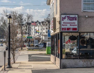 A view from up the street of Amy's Pizzeria. Further down the street are other houses, flags, and cars at an intersection.