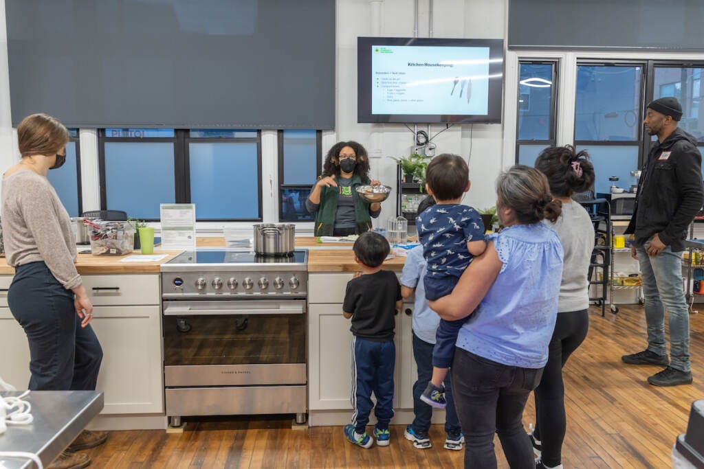 A group of people watch an instructor in a large kitchen.