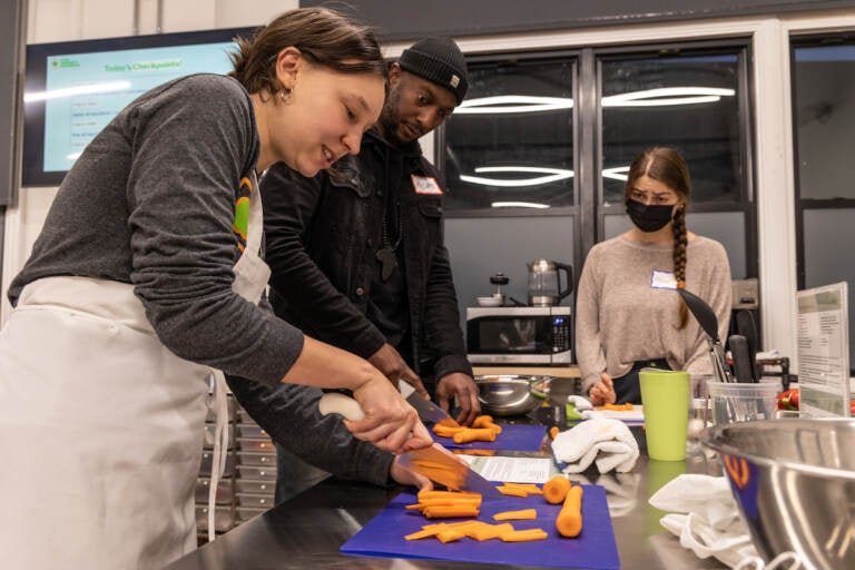 Roshan Basil watches as someone demonstrates how to julienne carrots.