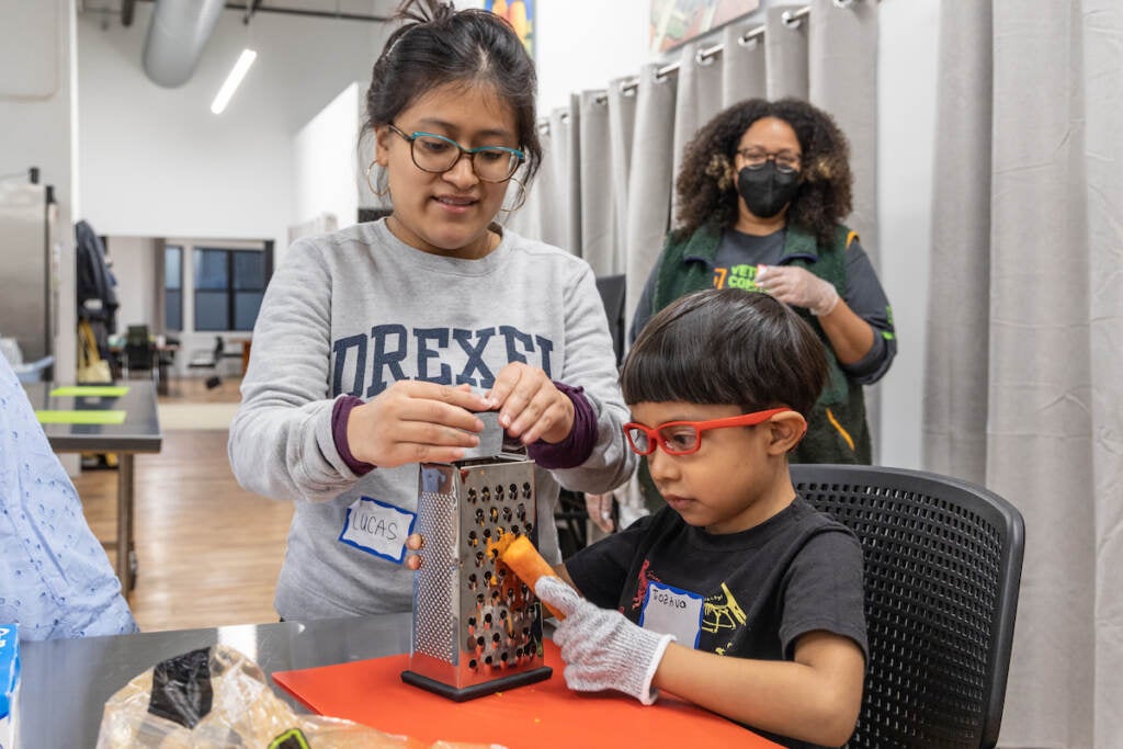 Martha Victoria (left) and her brother Joshua prep carrots for the community meal while instructor Erika Dorsey watches.