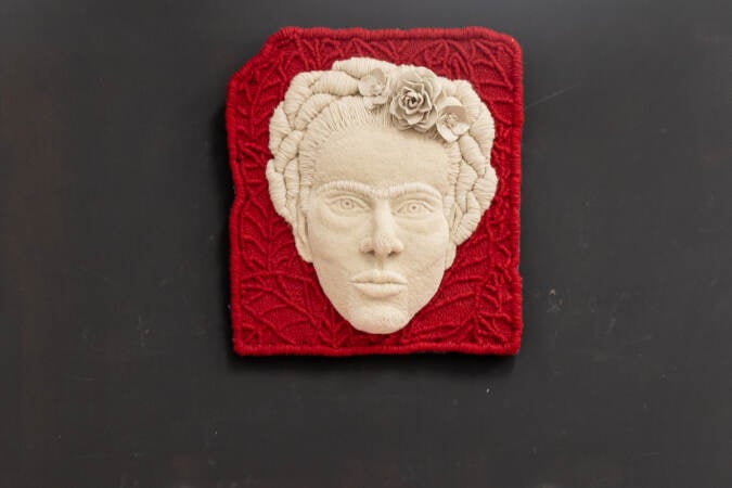A tufted portrait of Frida Kahlo is hung on a wall.