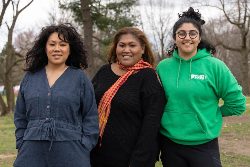 Catzie Vilayphonh, Kayla Sok, and Roxana Taginya pose for a photo. Trees and grass at FDR Park is visible behind them.