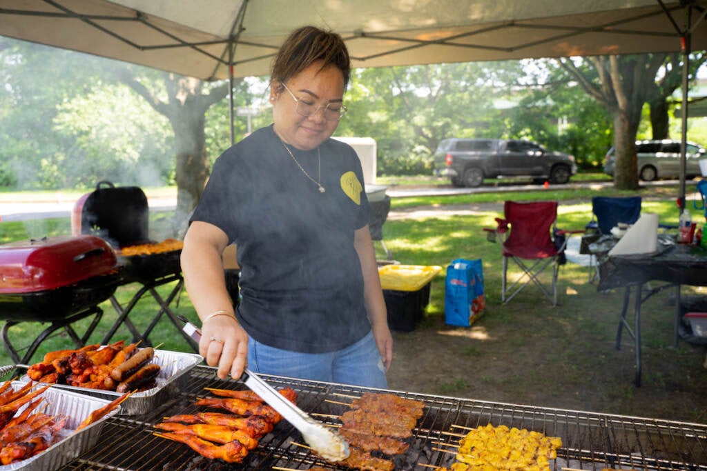 A vendor uses tongs to cook meat and other items on a grill in FDR Park.