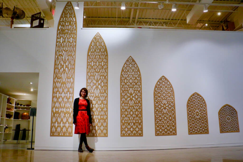 Nadia Kaabi-Linke stands next to an artwork installation displayed on the wall.