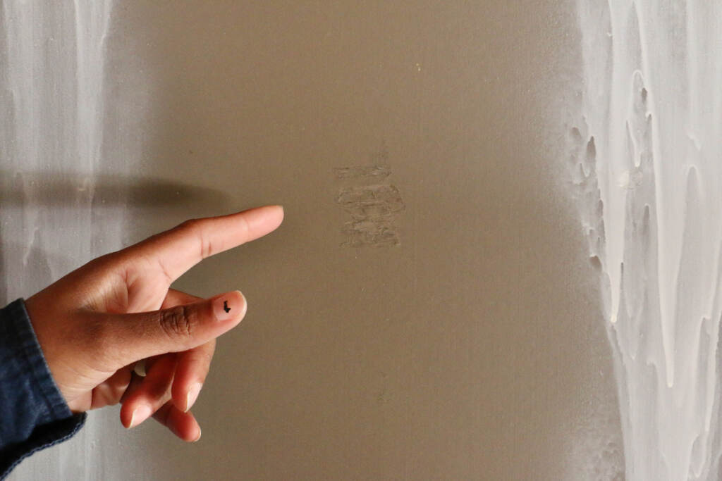 An up-close view of a hand pointing to a small dent in the wall.