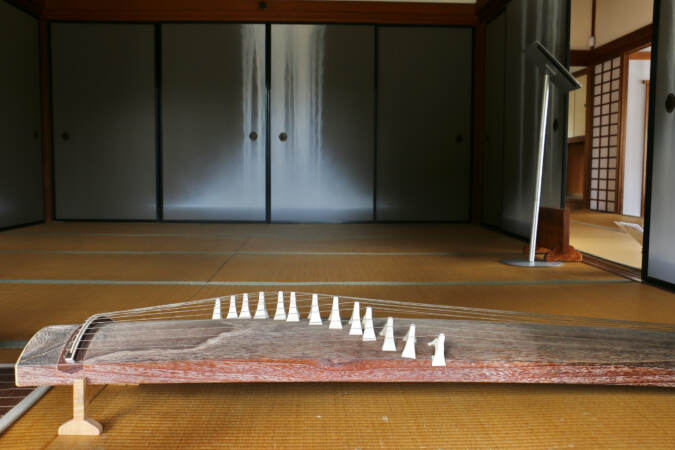 An up-close view of a koto, a Japanese string instrument, lying on tatami mats in an empty room.