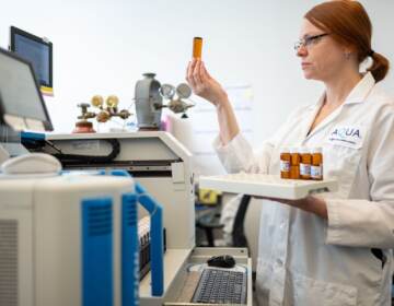 A scientist holds up a water sample at a testing station in a lab.