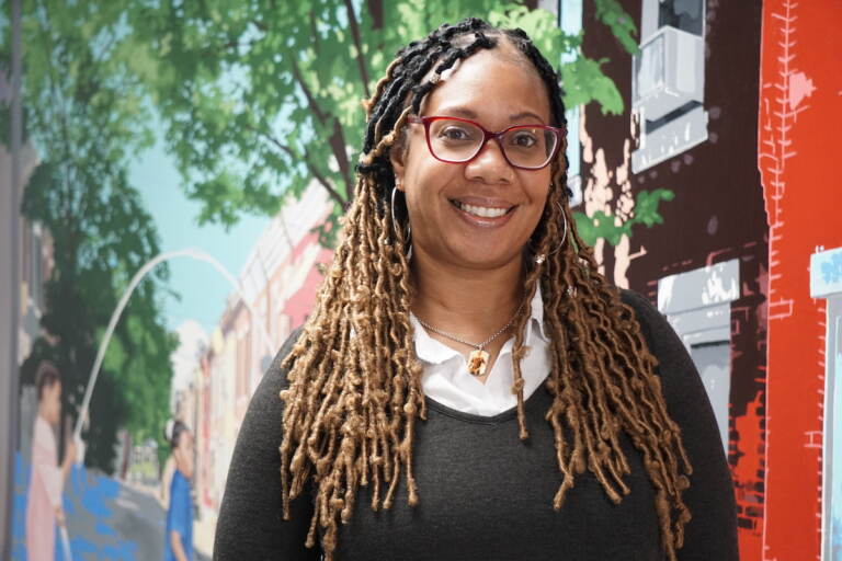 Maxayn Gooden smiles, posing for a photo in front of a mural.