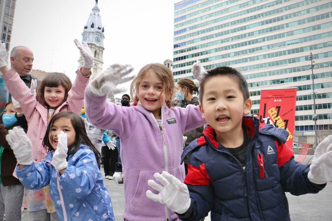 Children raise white-gloved hands as they participate in a community effort to break the world record for most people doing jazz hands at once during the kickoff of Philly Celebrates Jazz in Love Park