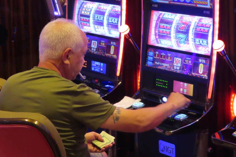 A person has a cigarette in their mouth while playing a slot machine.