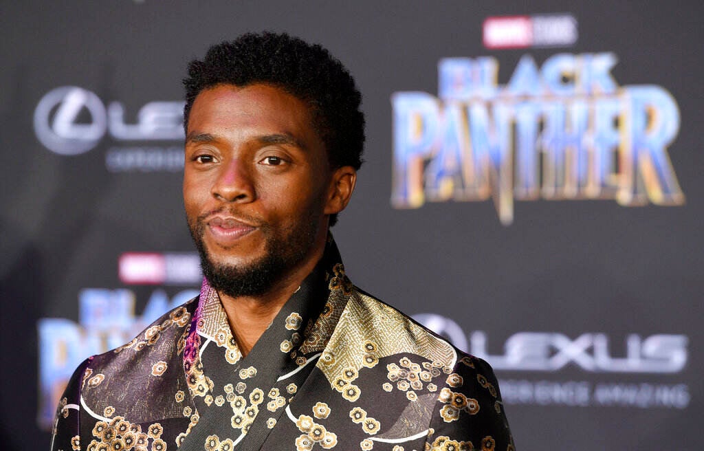 A close-up of Chadwick Boseman in front of a sign for "Black Panther: Wakanda Forever."