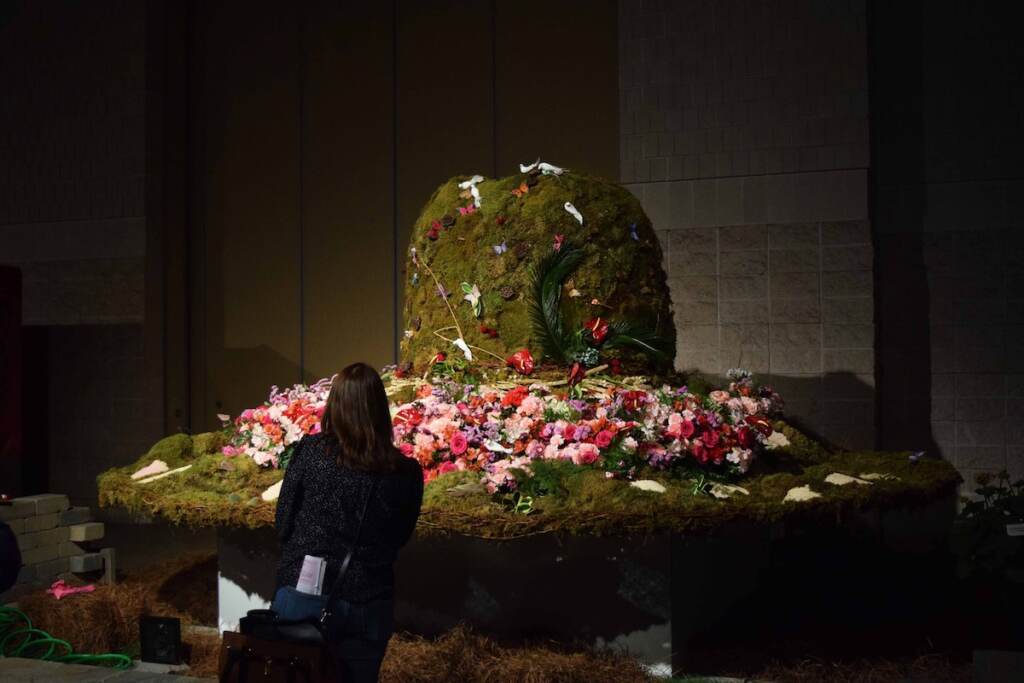 A large top hat is made with flowers and grass-covered earth.