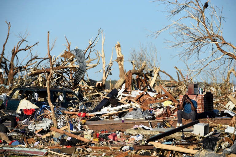 A man sits among the wreckage caused by a series of powerful storms and at least one tornado on March 25, 2023 in Rolling Fork, Mississippi