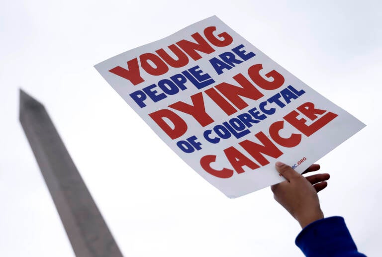 a person holding a sign that says 'Young people are dying of colorectal cancer'