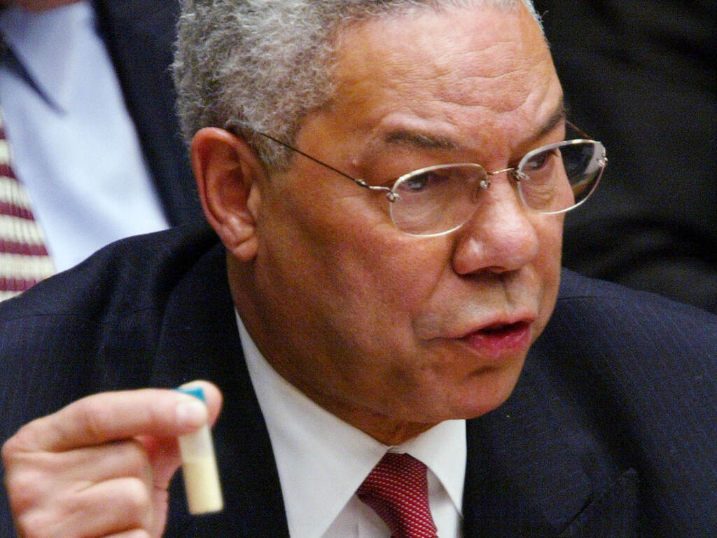 A close-up of Colin Powell holding a vial in his hand as he speaks.