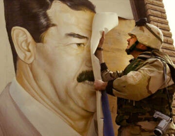 A soldier takes down a poster on a wall of Sadam Hussein.