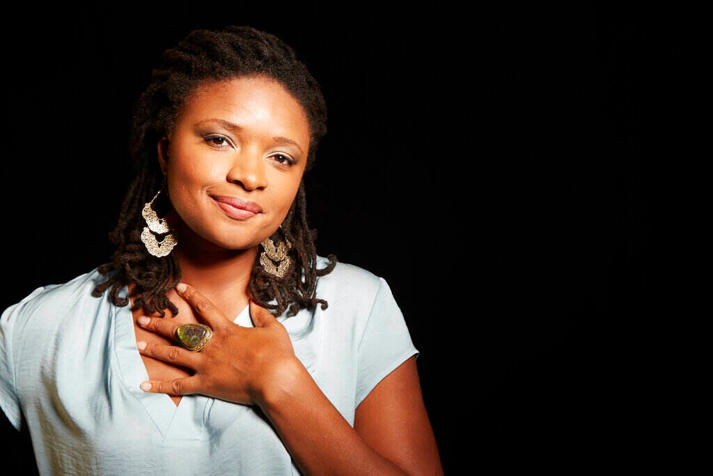 Lizz Wright poses for a photograph, with her hand over her heart, smiling slightly.