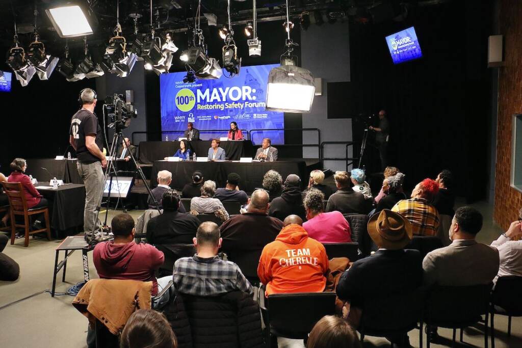 An audience watches mayoral candidates on a stage at a forum.