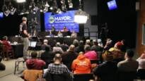An audience watches mayoral candidates on a stage at a forum.