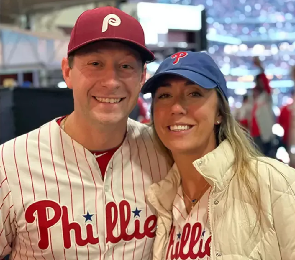 A man and woman wearing Phillies hats and jerseys
