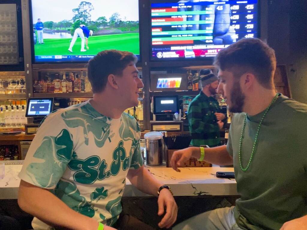 Joey McCool and his friend sit at a bar, both wearing green shirts.