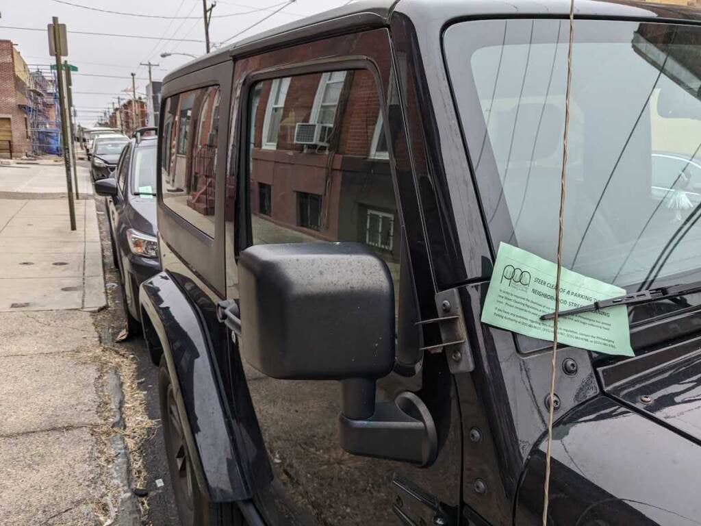 A green piece of paper is visible tucked into the windshield wiper of a car.