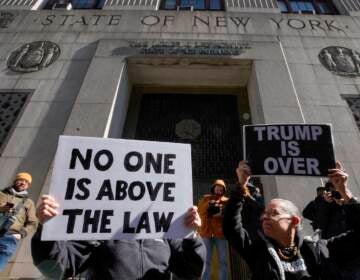 People hold up posters as part of a protest in front of the courthouse ahead of former President Donald Trump's anticipated indictment