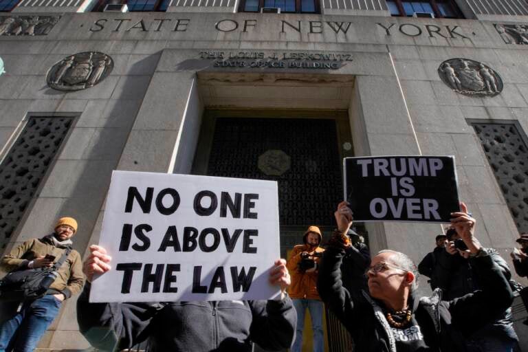 People hold up posters as part of a protest in front of the courthouse ahead of former President Donald Trump's anticipated indictment
