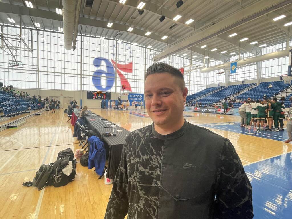 Steve Cavalier poses for a photo. Behind him is a basketball court.