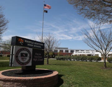 A view of a sign that reads Marple Newtown High School and a building on a sunny day.