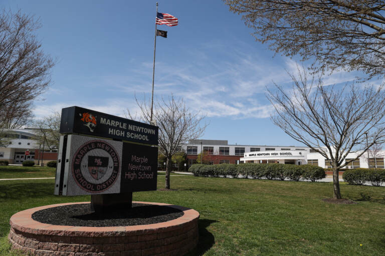 A view of a sign that reads Marple Newtown High School and a building on a sunny day.