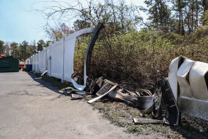 A fence that has been damaged by fire is visible alongside a forested area.