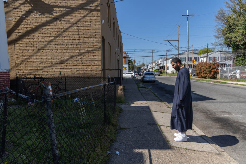 Anthony Freeman looks down towards the ground in front of a frontyard and a brick building.