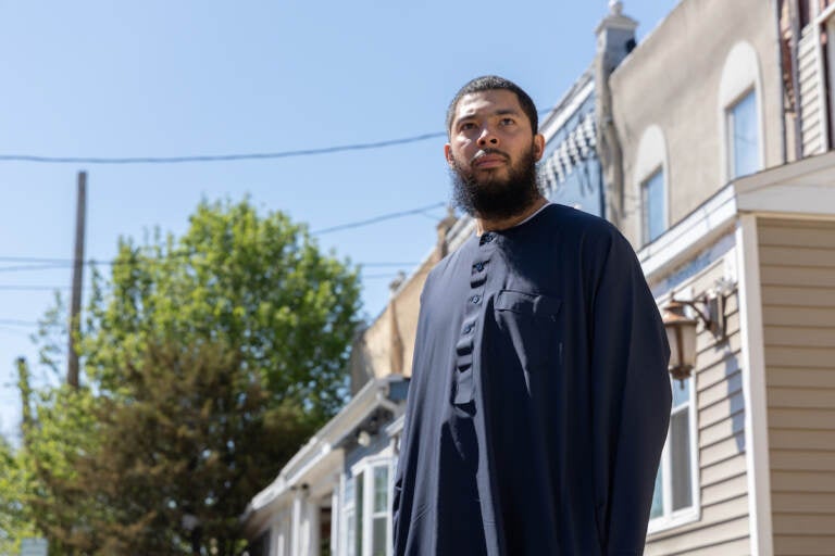 Anthony Freeman looks off into the distance. Behind him are trees and a row of houses.