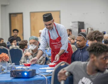 Madeel Abdullah, President National President, Ahmadiyya Muslim Youth Association serves participants small dishes of dates and spicy chickpeas which are eaten as part of breaking the fast during an Interfaith Iftar at the Baitul Aafiyat Mosque