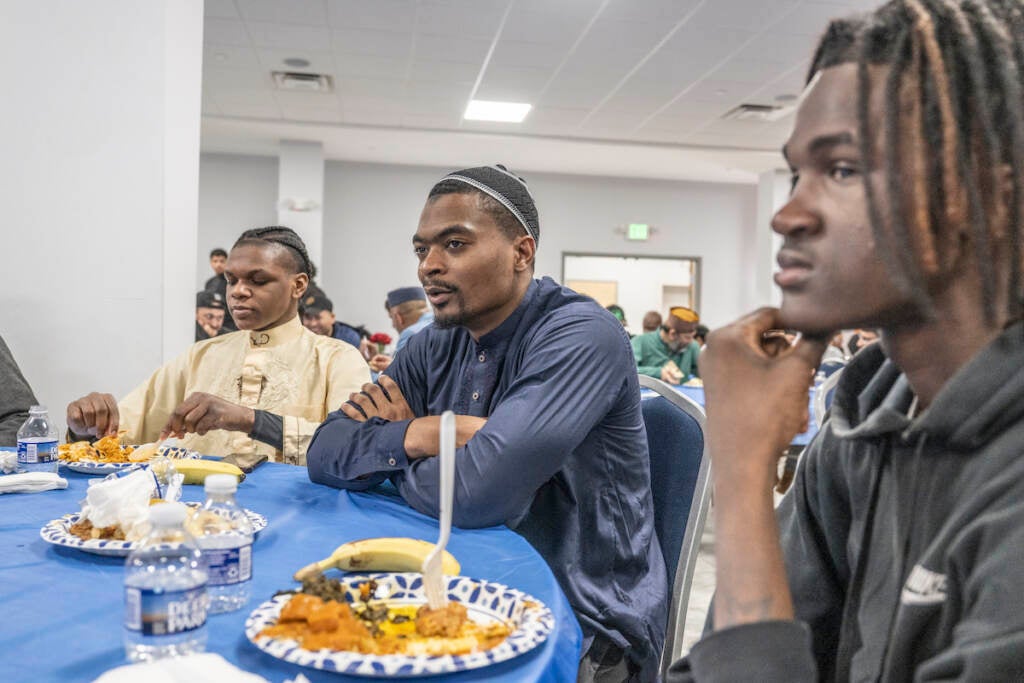 Youth mentor Jaheim Thomas (center) shares a meal with young members of the Baitul Aafiyat Mosque at the conclusion of Interfaith Iftar on Saturday evening. On left is Azyir Worsham and on the right is Jamil Wright