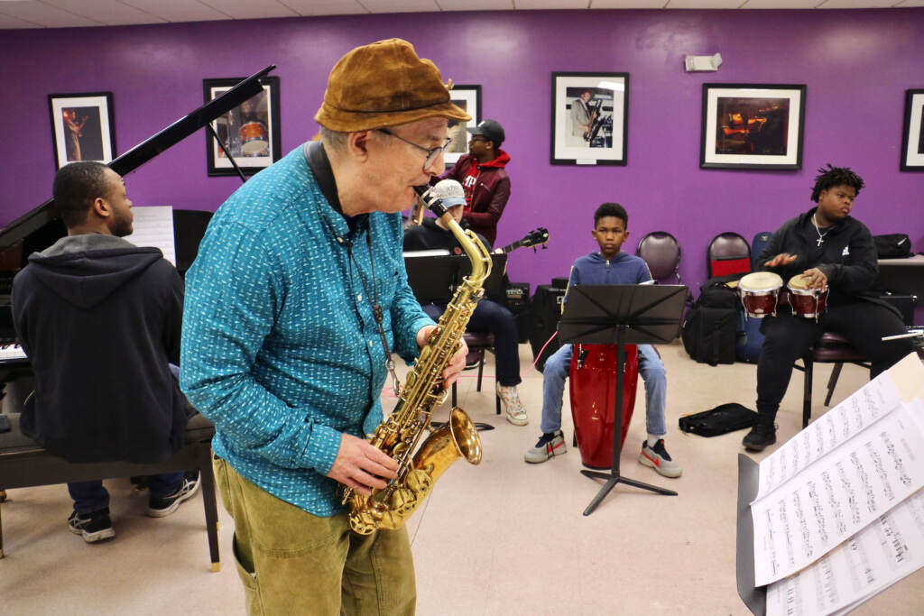 Bobby Zankel plays the saxophone as students look on.