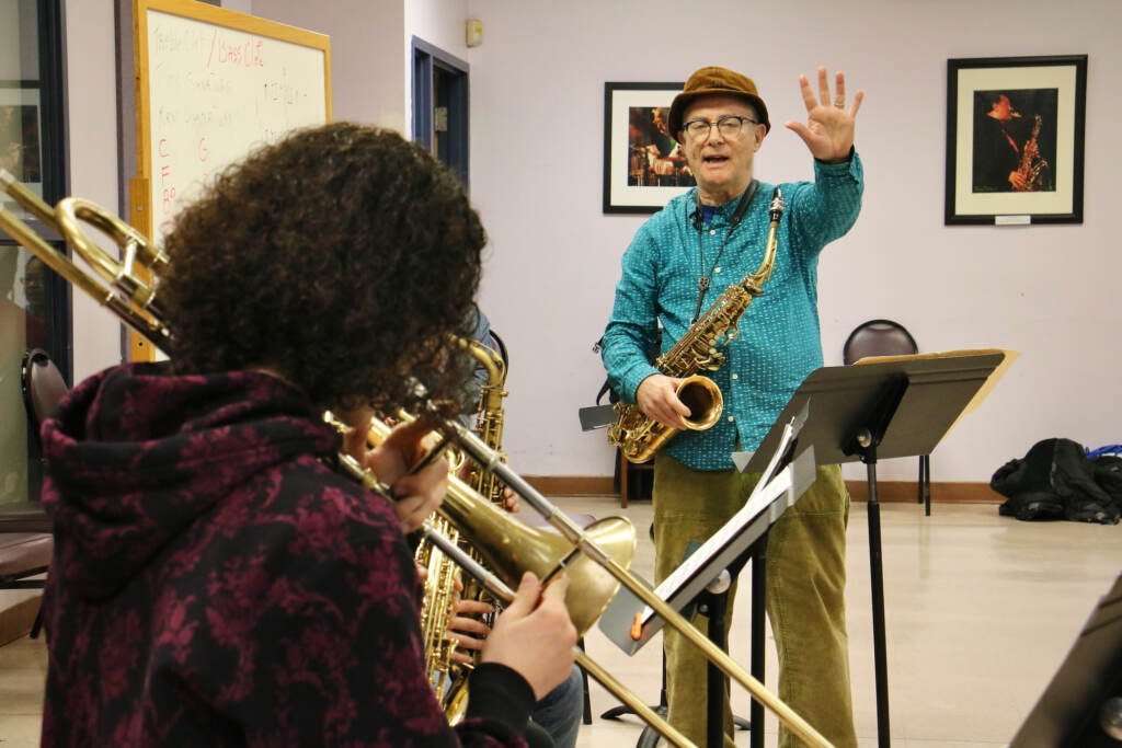 Bobby Zankel holds up his hand. A student in the foreground plays an instrument.