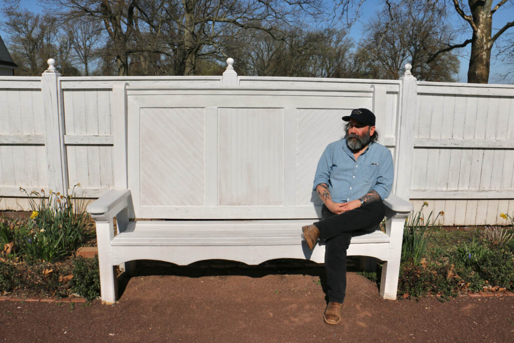 Artist Nathan Young sits on one of four benches that are a part of his immersive installation on the grounds of Pennsbury Manor. Sound emmanates from the back of the bench without any visible speakers