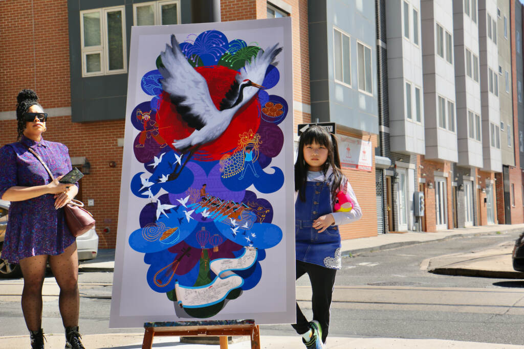 Angela Wei stands next to an easel showing a replication of a mural.