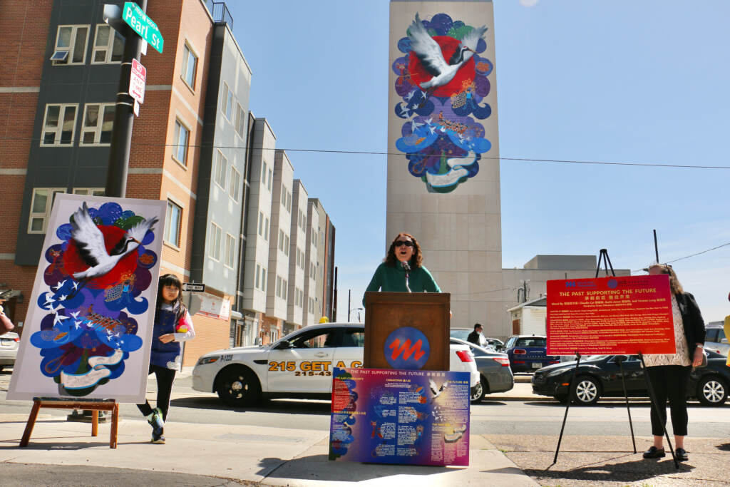 Jane Golden speaks at a podium in front of a mural.